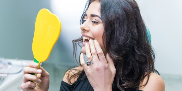 a woman checking her teeth in a yellow mirror after a whitening treatment, admiring the bright results