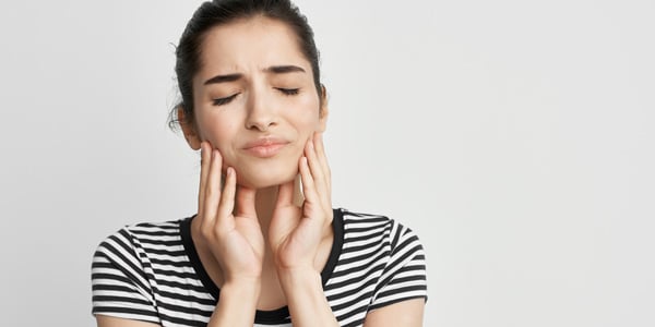 a woman in a striped shirt feeling toothache, holding her cheek in discomfort