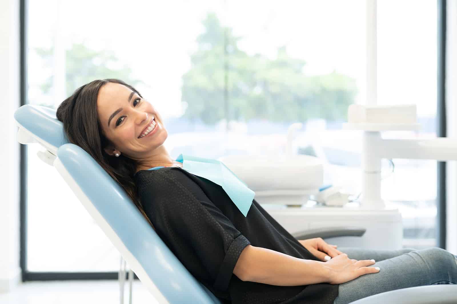 a woman in a black shirt comfortably lying on a dental clinic chair, showcasing her confident smile